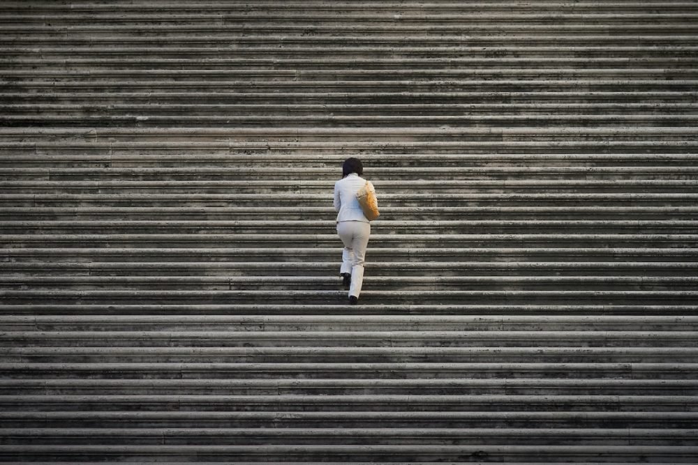 图片:一个孤独的女人走上一组巨大的楼梯,楼梯从画框的四周延伸出去。