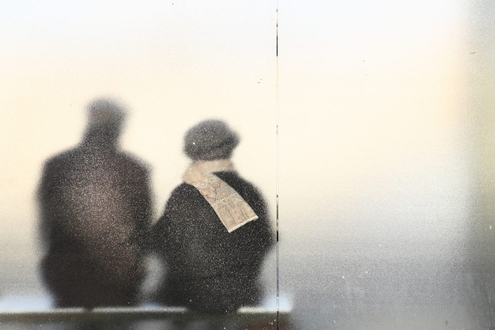 图片：一对夫妇的剪影坐在公交车站，从后面通过磨砂玻璃看到。