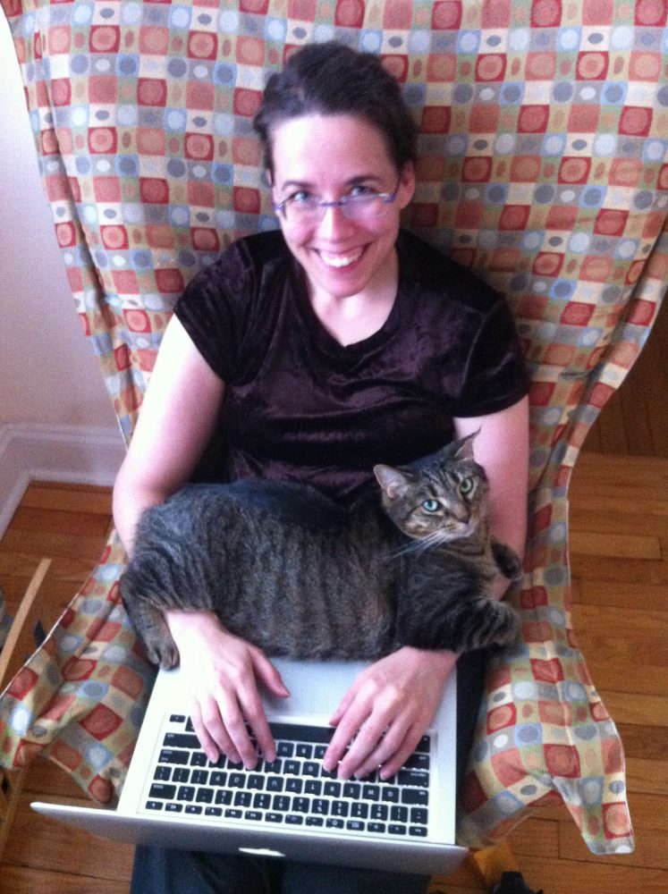 图片：简·弗里beplay体育sports德曼坐在椅子上，用笔记本电脑打字；一只名叫塞尔达的猫伸过她的胳膊。