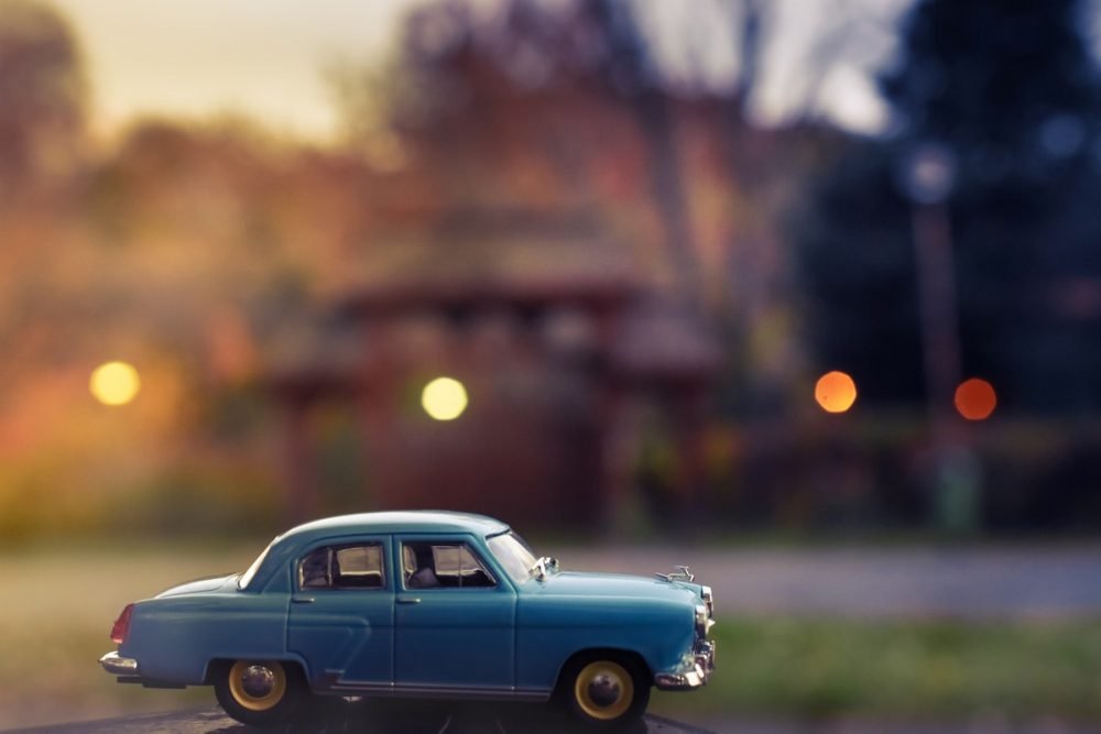 图片：一个微型古董汽车的特写镜头照片在前景的，与被弄脏的城市街道在背景中。