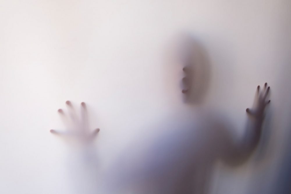 图片：一个模糊的图形的手和脸在白色屏幕后面。