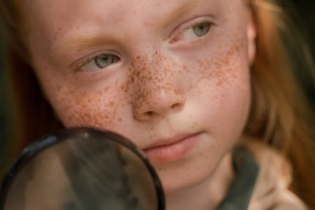 图片：一个年轻，红头，雀斑的女孩，拿着放大镜。
