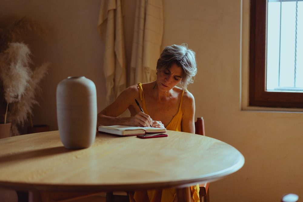 图片：一个桌子上的女人，在日记中写作。