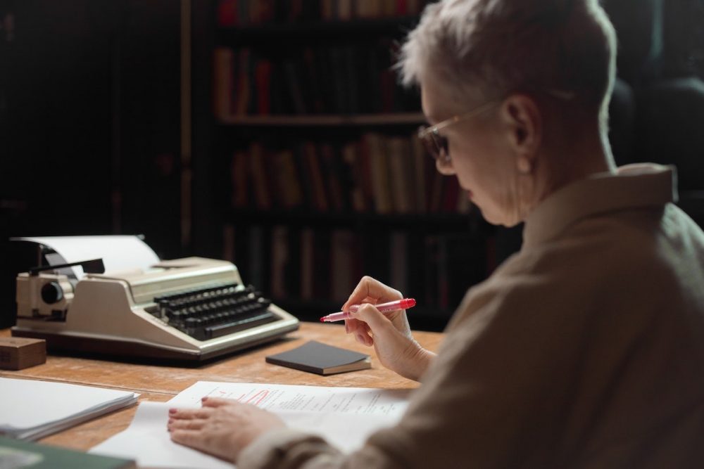 图片：一个坐在桌子上的女人，用红笔编辑手稿。