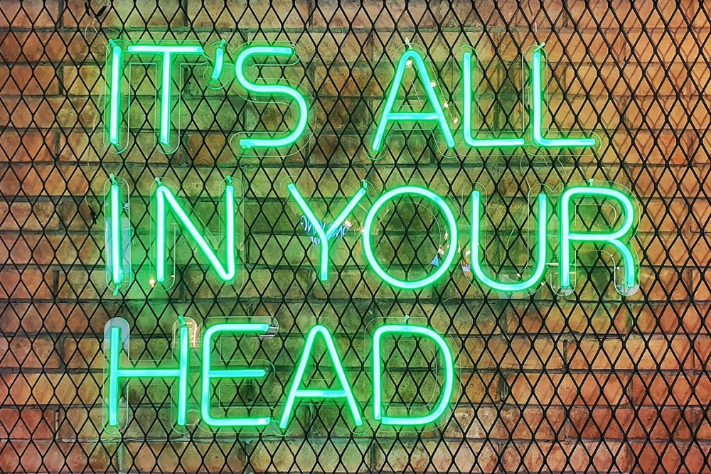 图片:一个绿色的霓虹灯标志，上面写着“一切都在你的脑海中”，安装在一个金属网架上，靠在一堵砖墙上。