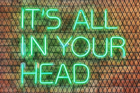图像：绿色的霓虹灯标志阅读“全部在您的脑海中”被安装在砖墙上的金属网格框架上。