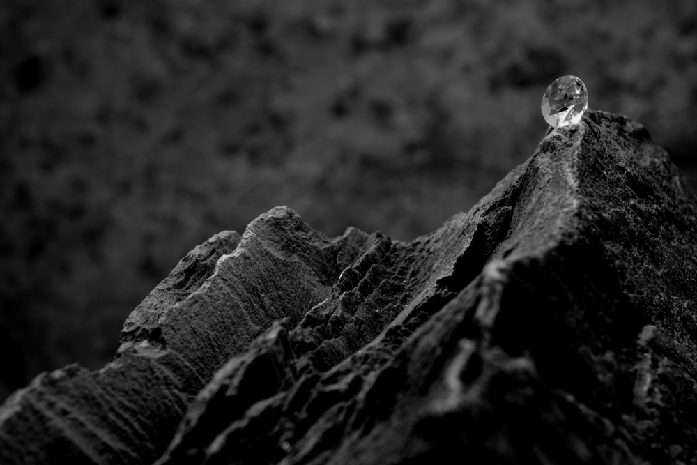 图片:一颗切割过的钻石放在一堆黑色岩石上。