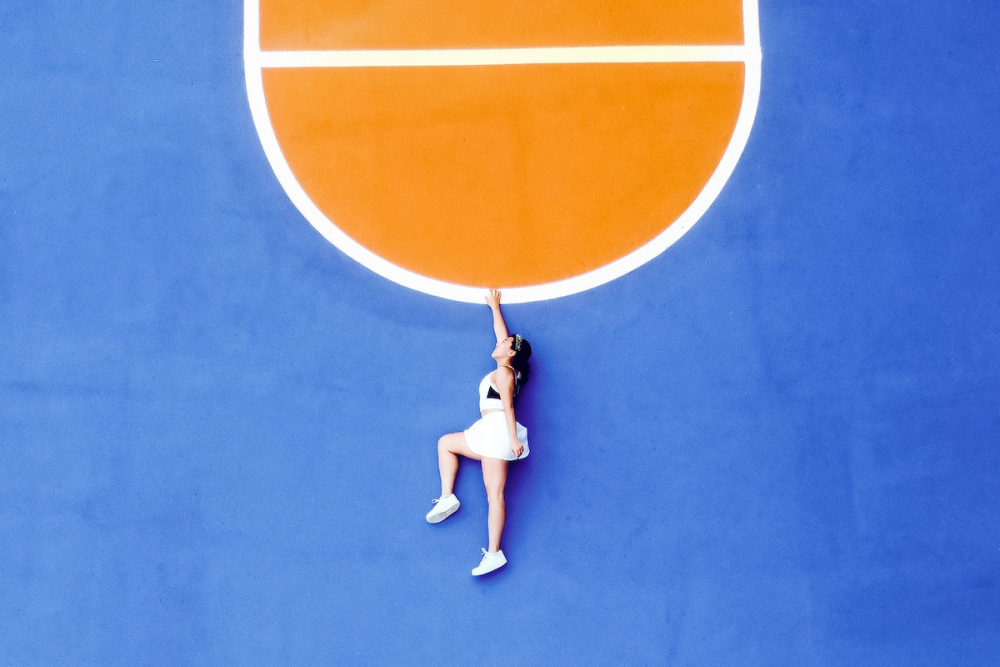 图片:鸟瞰图，一个穿着运动服的女人躺在体育馆的地板上。从这个角度看，她似乎是挂在画在地板上的半圆形线上。