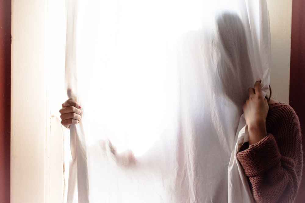 图片:一个女人躲在窗帘后面，只看得见她的手和肩膀。