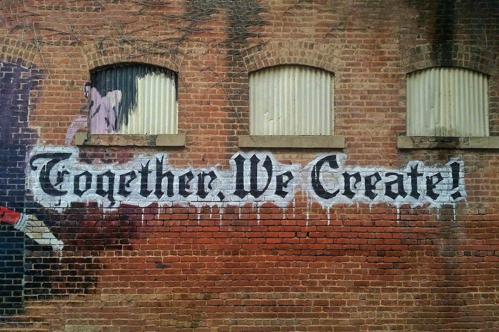 图片:一个废弃工厂的外墙砖墙，上面画着一幅壁画，写着“一起创造!”