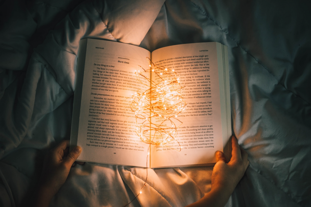 图片:在一个黑暗的房间里，有人在床上拿着一本书。在打开的书页上，有一堆杂乱的发光led灯。