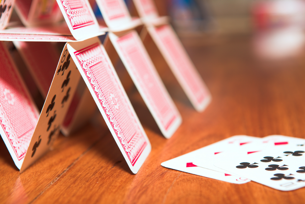 图片:用木桌上摇摇欲坠的扑克牌堆成的房子。
