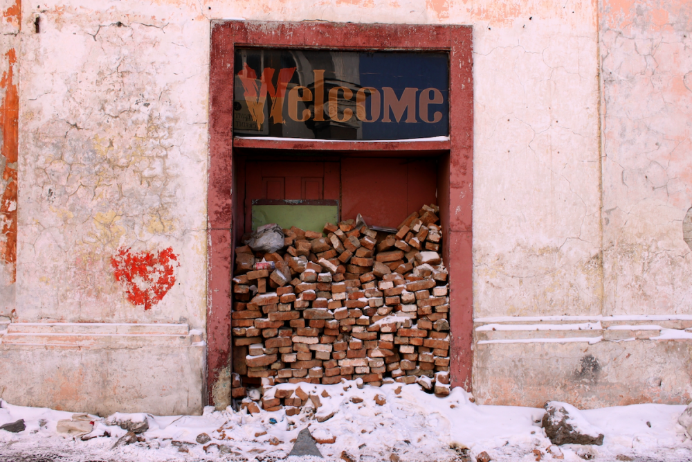 图片:一座破旧建筑的门口堆着砖头，阻止人们进入。门口上方有一个大牌子，上面写着“欢迎光临。”