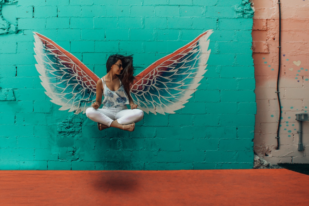 图片:一双彩色的翅膀是画在一块砖头墙。似乎漂浮空中的翅膀,仿佛他们属于她,一个女人坐在crosslegged。