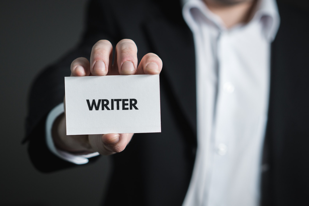 图片:一名穿着职业装的男子拿出一张名片，上面只印着“作家”两个字。