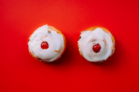 图片:在一个红色的桌面是两个并排肉桂卷,每个泛起白色糖衣和切片樱桃,联想到像一对乳房。