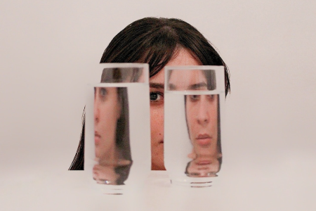 图片:一个年轻女子的脸是透过两杯水,这样图像分裂成多个角度。